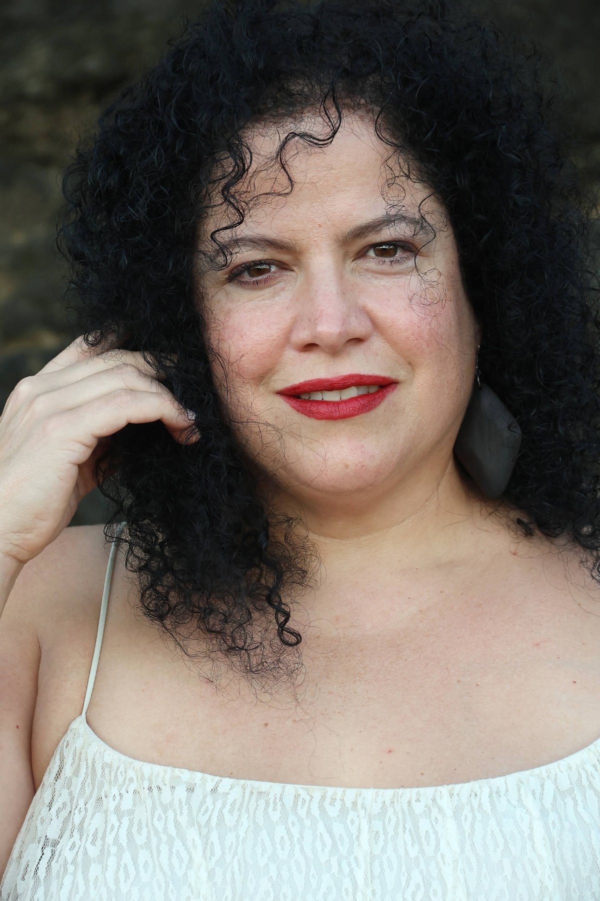 Geña in a white dress beside a dark stone wall