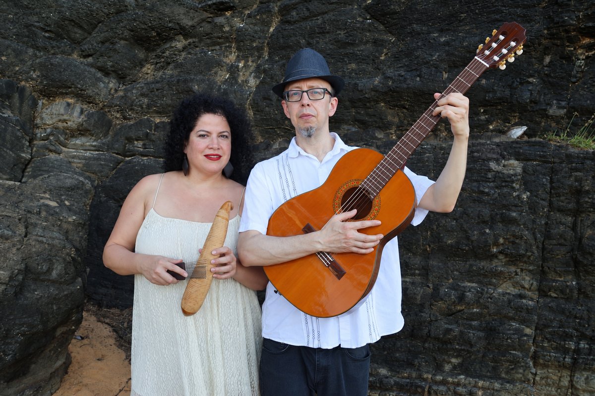 Geña with percussion beside Carlos Peña holding his guitar against a stone wall
