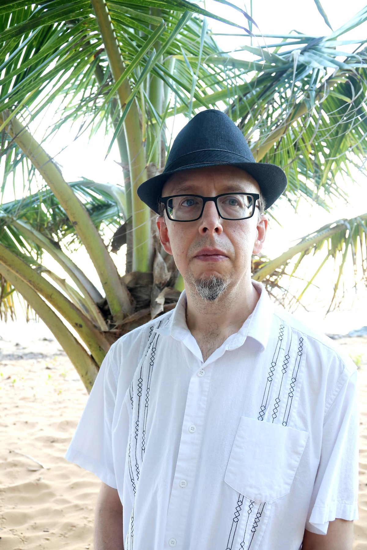 Carlos Peña wearing a hat and glasses beneath palm leaves