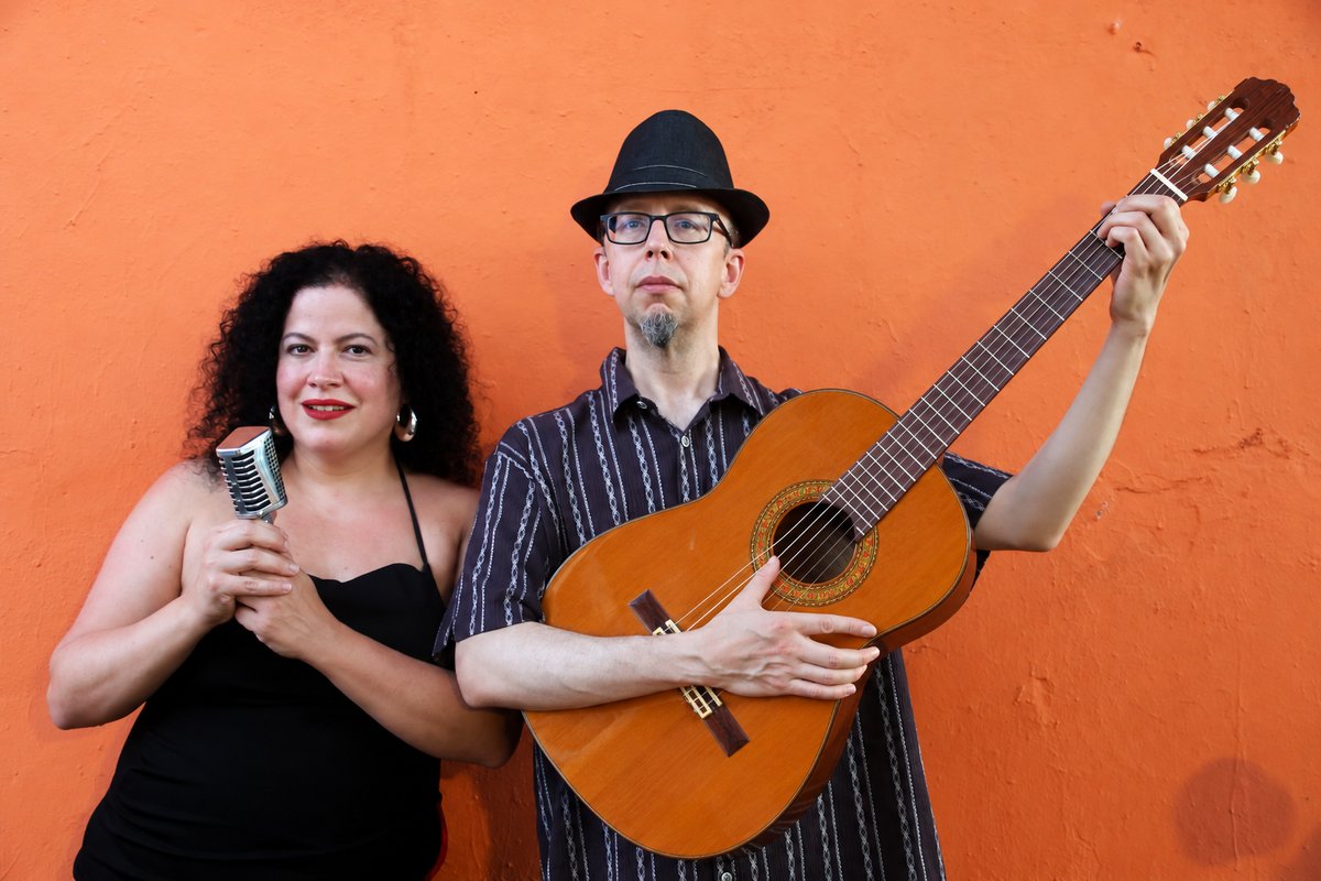 Geña at a vintage microphone beside Carlos Peña with his guitar